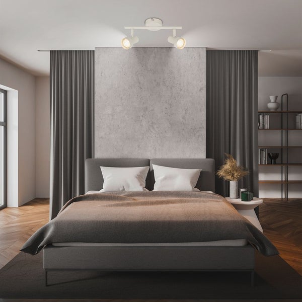 Zweiflammiger Deckenstrahler in einem modern eingerichteten Schlafzimmer mit Doppelbett, Sichtbetonwand und grauen Vorhängen.