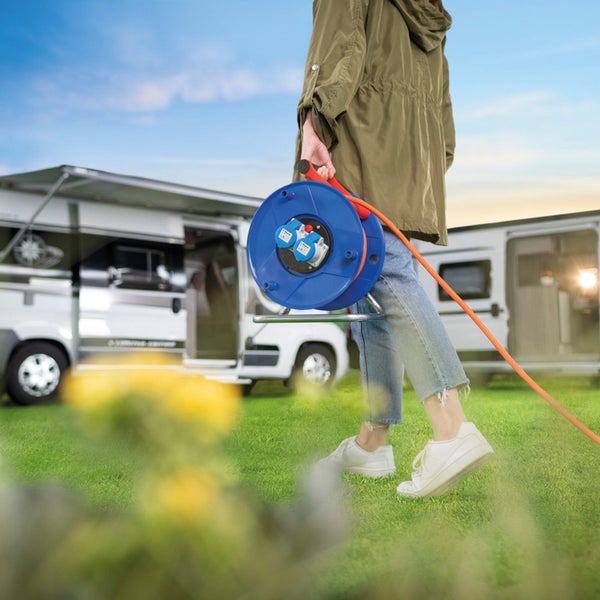 Person hält eine Kabeltrommel mit CEE Stecker auf einem Campingplatz.