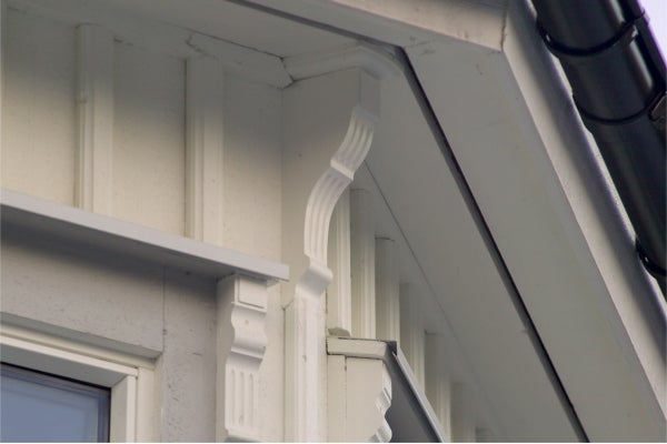 Dekorative Holzzierleiste als architektonisches Element an einer Hausfassade im Landhausstil unter dem Dachvorsprung.