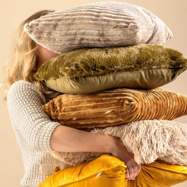 Eine Person hält einen Stapel verschiedener Dekokissen mit Oberflächen aus Cord und Kunstfell.