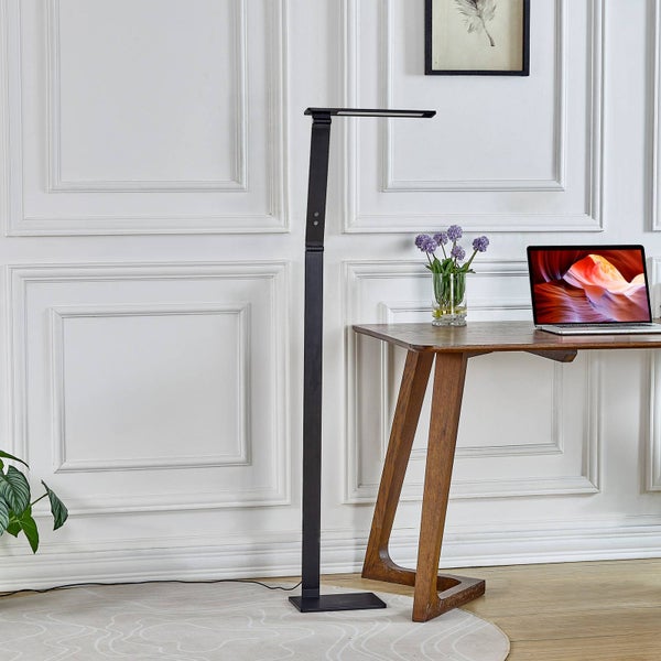 Moderne schwarze Stehleuchte aus Metall in einem hellen Arbeitszimmer neben einem Holzschreibtisch mit Laptop und lila Blumen.