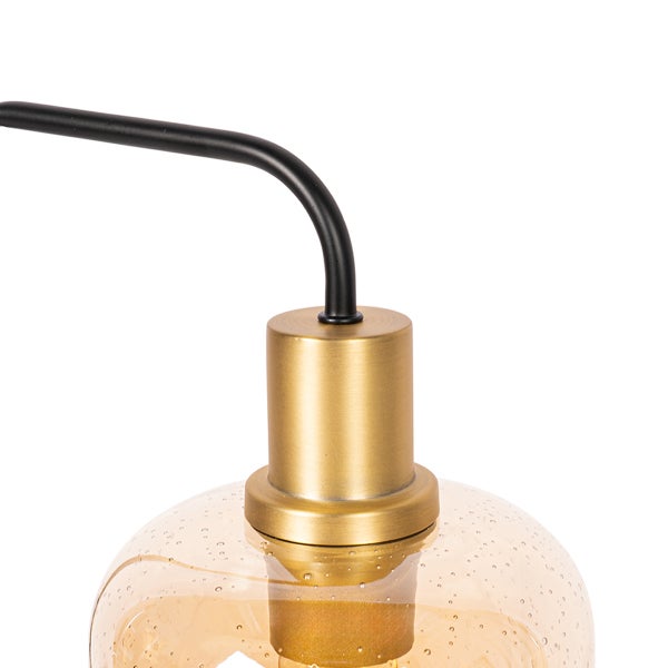 Detailaufnahme einer Leuchte mit gebogenem schwarzem Metallarm, Fassung in Messingoptik und einem Lampenschirm aus strukturiertem Glas.