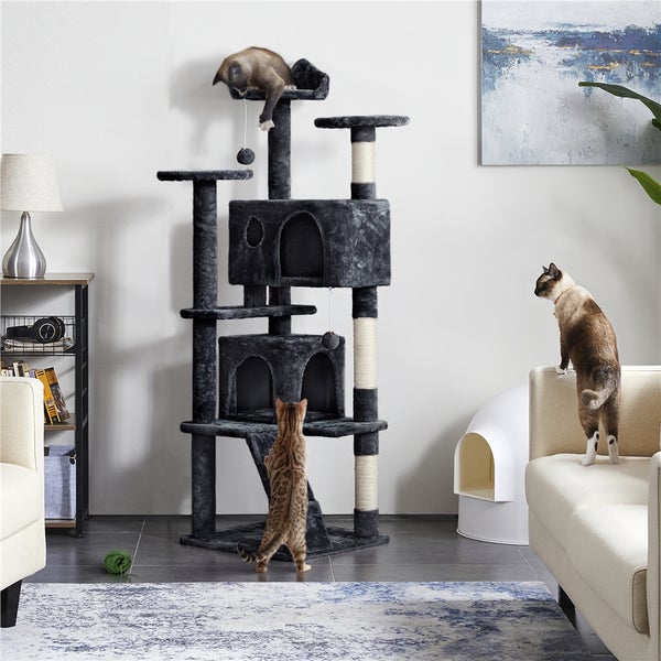 Kratzbaum mit mehreren Ebenen, Höhlen und Spielzeugen in einem hellen Wohnzimmer mit Katzen.