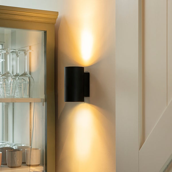 Moderne schwarze zylindrische Wandleuchte an einer Wand neben einem Glasschrank, die warmes Licht nach oben und unten strahlt.