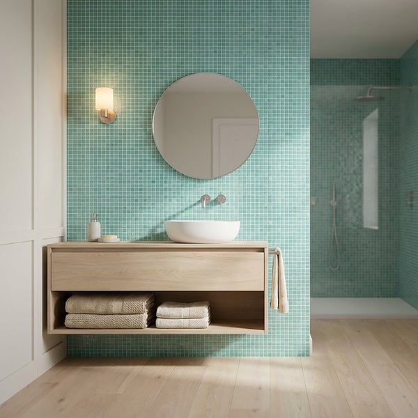 Modernes Badezimmer mit Mosaikfliesenwand, hängendem Holzwaschtisch, weißem Aufsatzwaschbecken und rundem Spiegel in einer organisierten Umgebung.