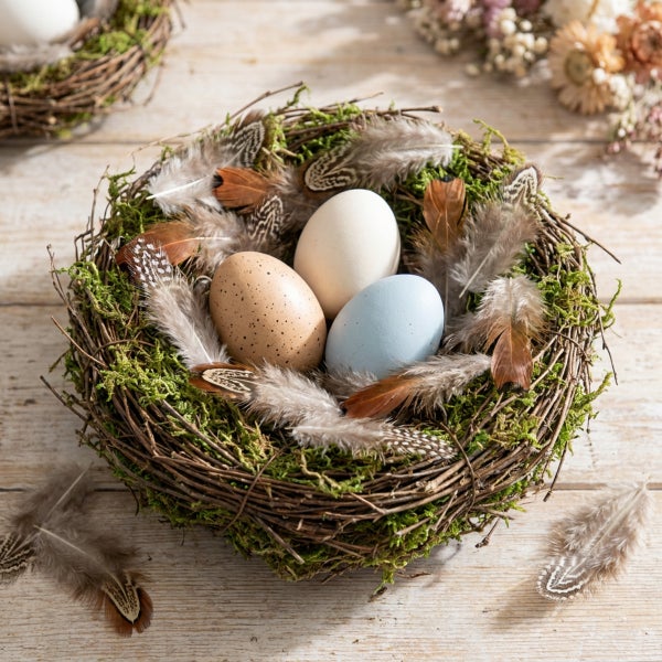 Osternest aus Zweigen und Moos mit drei Deko Eiern und Federn auf einem Holztisch dekoriert