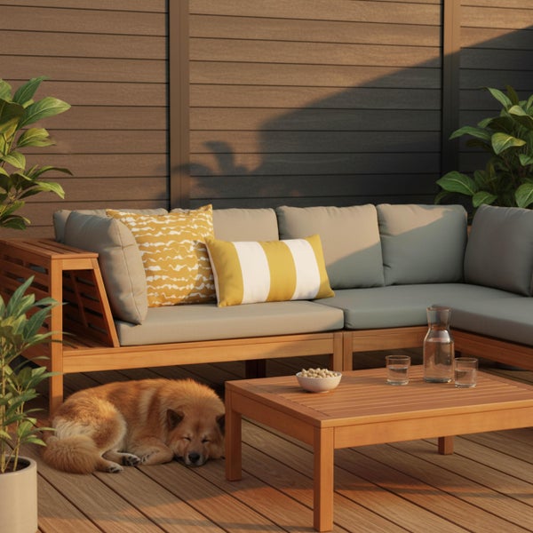Helles Loungemöbel-Set aus Holz mit grauem Ecksofa, Couchtisch und gelben Kissen auf einer organisierten Holzterrasse vor einem Sichtschutzzaun.