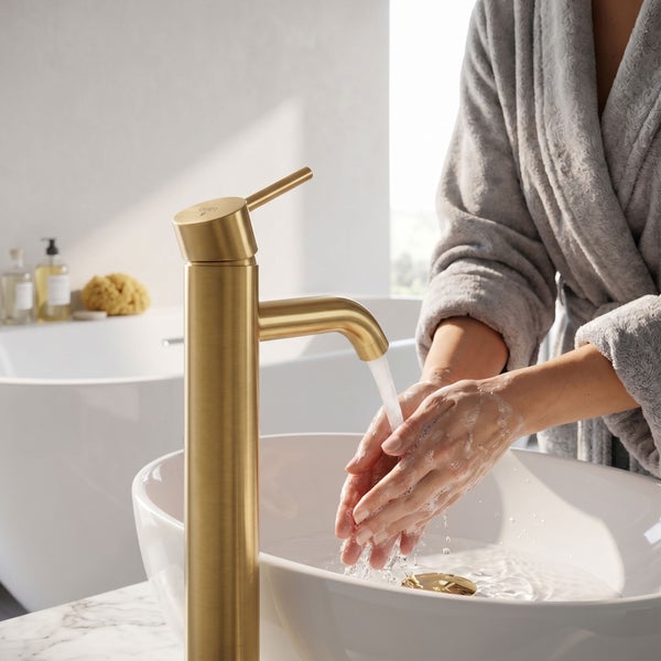 Hände waschen in einem weißen Aufsatzwaschbecken unter einer hohen, goldfarbenen Armatur in einem hellen Badezimmer.