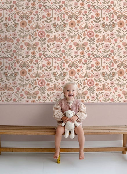 Mädchen sitzt vor einer Wand mit floraler Schmetterlingstapete auf einer Holzbank
