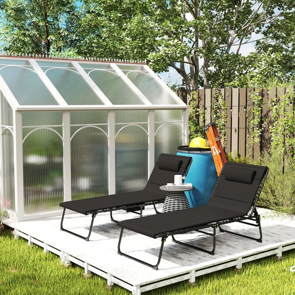 Zwei schwarze Gartenliegen auf einer hellen Holzterrasse vor einem weißen Gewächshaus in einem sonnigen Garten.