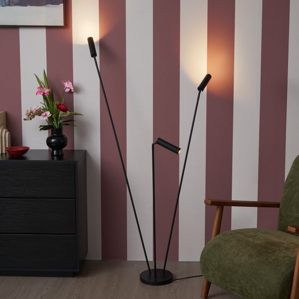 Schwarze dreiarmige Stehleuchte aus Metall in modernem Wohnzimmer neben einer Kommode und einem Sessel.
