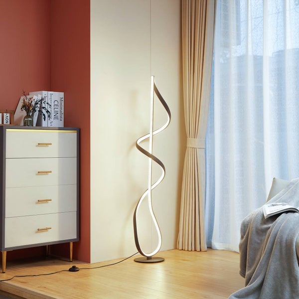 Moderne LED-Stehleuchte in Spiralform in einem hellen Wohnzimmer neben einer Kommode und Vorhängen.