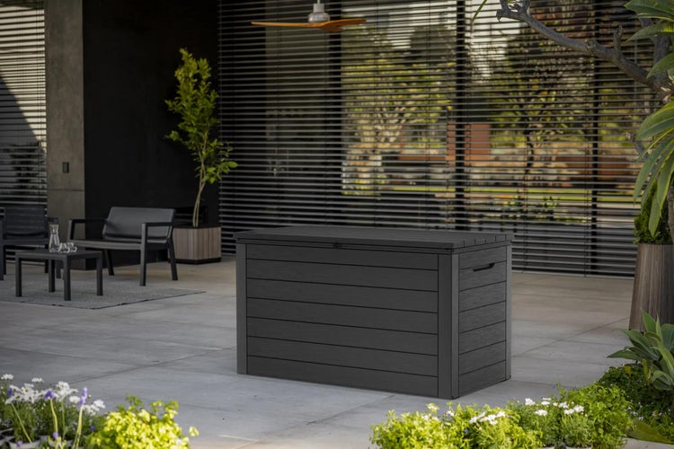 Moderne Gartenbox in Anthrazit mit Holzoptik auf einer Terrasse, umgeben von Gartenmöbeln und Pflanzen.