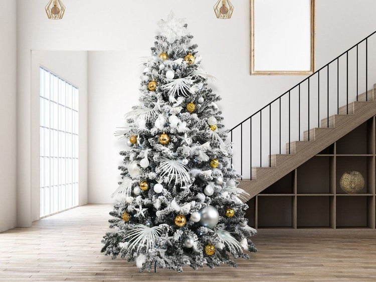 Ein künstlicher, verschneiter Weihnachtsbaum, geschmückt mit Kugeln und Elementen in einer modernen Wohnumgebung mit Treppe im Hintergrund.