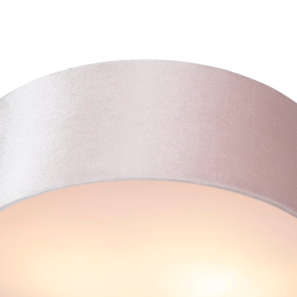 Nahaufnahme eines runden Lampenschirms aus hellrosa Stoff mit feiner Textur und Lichtschein.