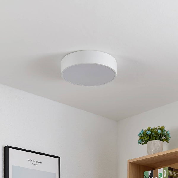 Rundes weißes Deckenlicht an einer weißen Decke in einem hellen, organisierten Zimmer mit Wandbild und Bücherregal.