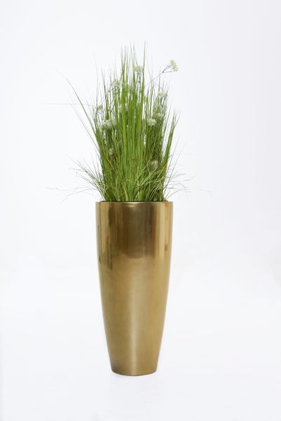 Künstliche Gräser mit weißen Blüten in einer hohen goldfarbenen Bodenvase.