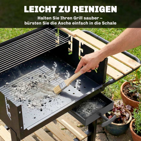 Eine Hand fegt mit einem Pinsel Asche aus der Wanne eines schwarzen Holzkohlegrills in die ausziehbare Ascheschale.