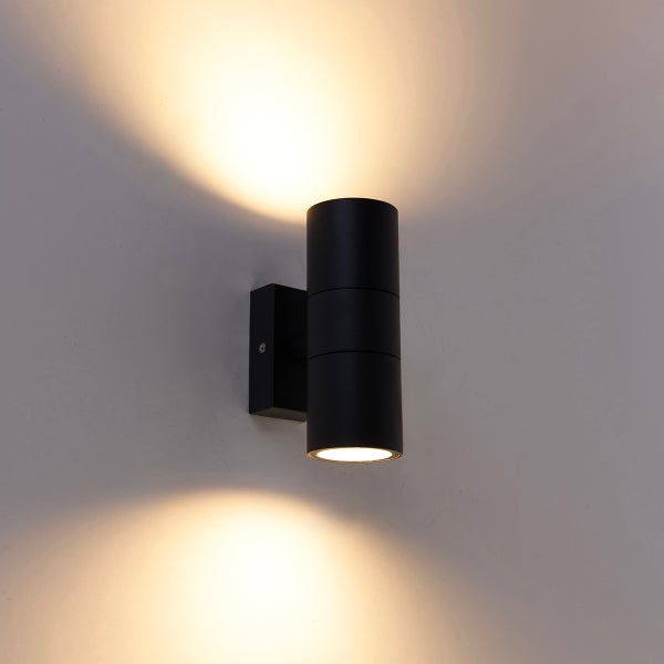 Schwarze, zylindrische Wandleuchte mit Lichtaustritt nach oben und unten an einer Wand.