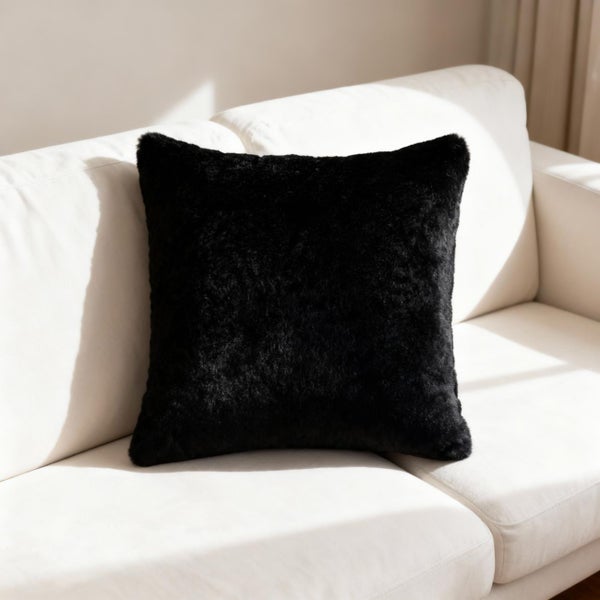 Schwarzes Kunstfellkissen mit weicher Textur auf einem hellen Sofa in einem hellen Wohnzimmer.