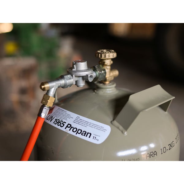 Gasdruckregler montiert an einer grauen Propangasflasche mit angeschlossenem orangefarbenem Gasschlauch.