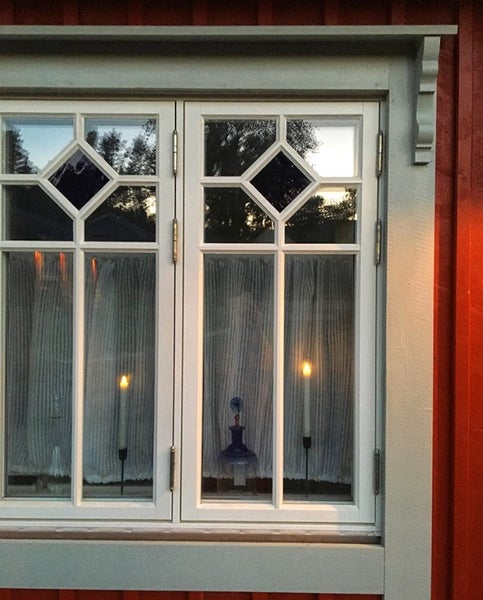 Zweiflügeliges Sprossenfenster mit dekorativen Rauten im oberen Bereich und verzierten Fensterleibungen an einer roten Fassade.