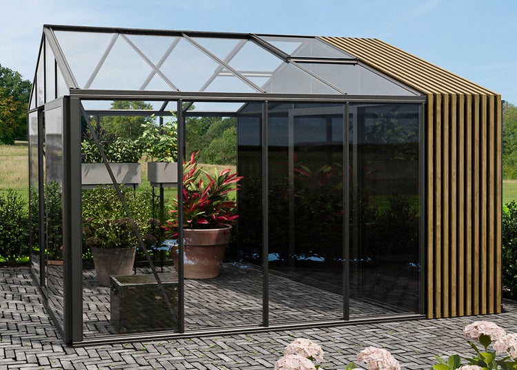 Modernes Gewächshaus mit Glaswänden, Metallrahmen und Holzlattenwand auf einer Terrasse. Im Inneren befinden sich Pflanzen in Töpfen.