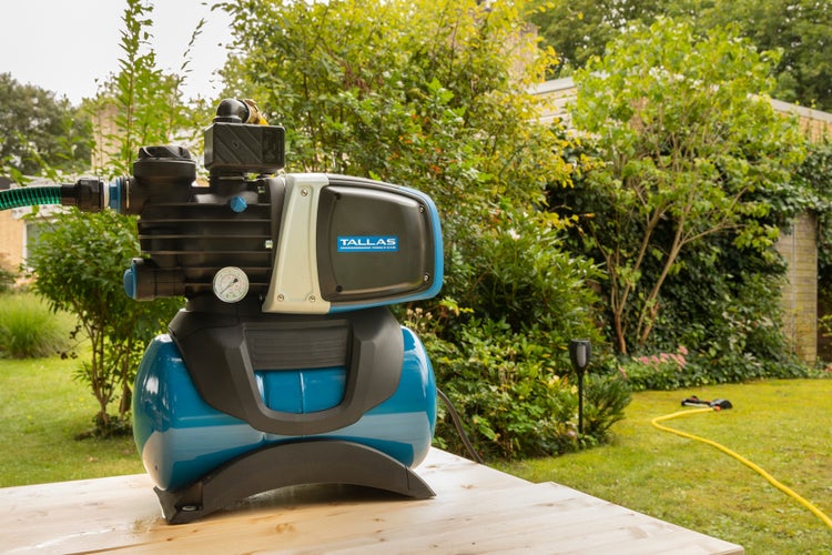 Hauswasserwerk auf Holztisch im Garten. Tallas Logo.
