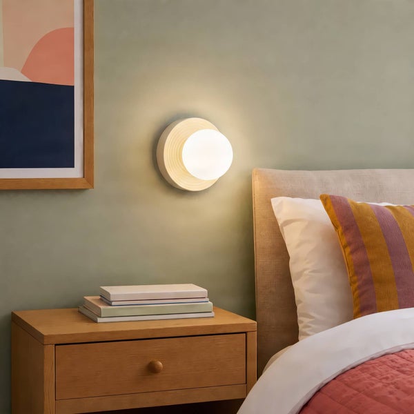 Moderne runde Wandleuchte mit leuchtender Glaskugel montiert über einem Nachttisch in einem Schlafzimmer.