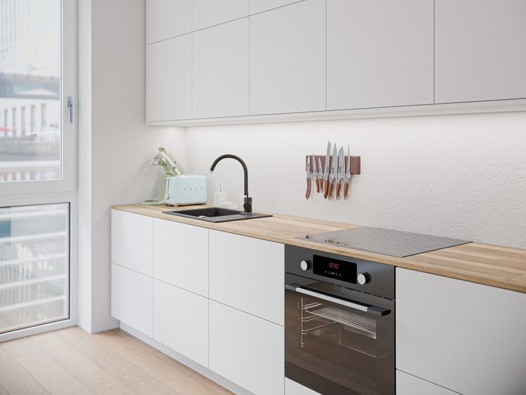 Moderne, helle Küche mit weißen Schränken, Holz-Arbeitsplatte, schwarzem Spülbecken, Einbauofen und magnetischer Messerleiste.