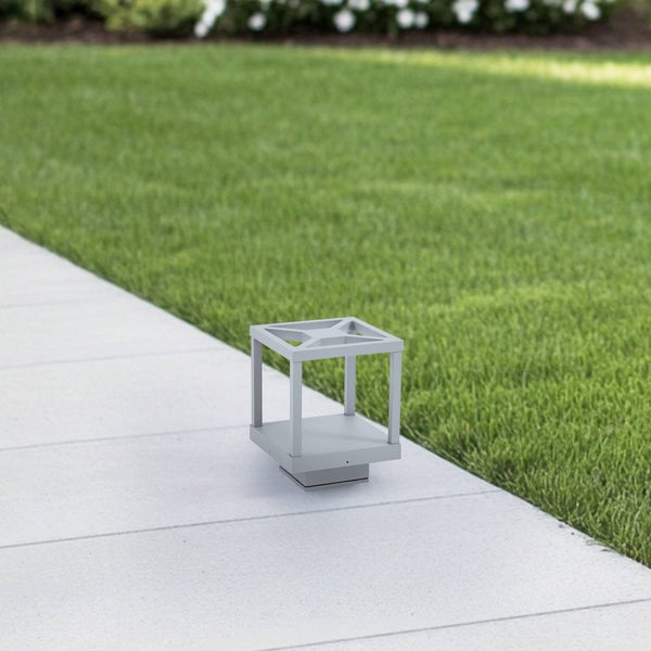 Moderne, graue Außenleuchte in Würfelform aus Metall auf einem hellen Steinweg neben einer grünen Rasenfläche.