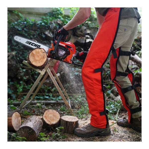 Eine Person schneidet mit einer Kettensäge einen Holzstamm auf einem Sägebock und trägt Schnittschutz-Beinschutz.