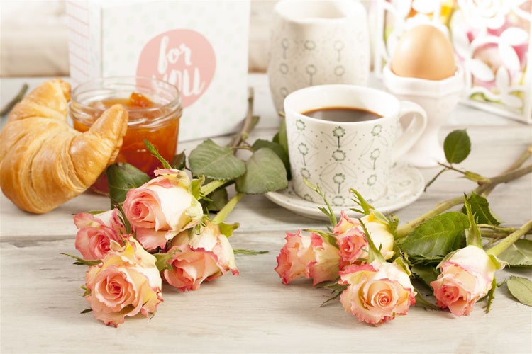 Frühstücksszene mit Croissant, Marmelade, Kaffee, gekochtem Ei und Rosen auf einem Tisch