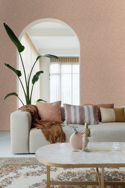 Wohnzimmer mit beiger Couch, Kissen, Decke, Tisch und gemusterter Tapete