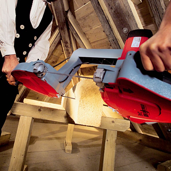 Handwerker verwendet Mafell Bandsäge zum Schneiden eines Holzbalkens auf einem Dachboden.