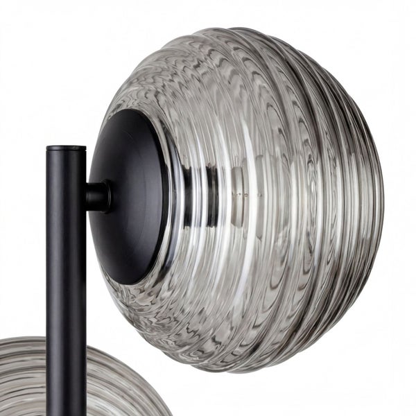 Nahaufnahme einer Leuchte mit schwarzem Metallgestell und rundem, geriffeltem Glasschirm.