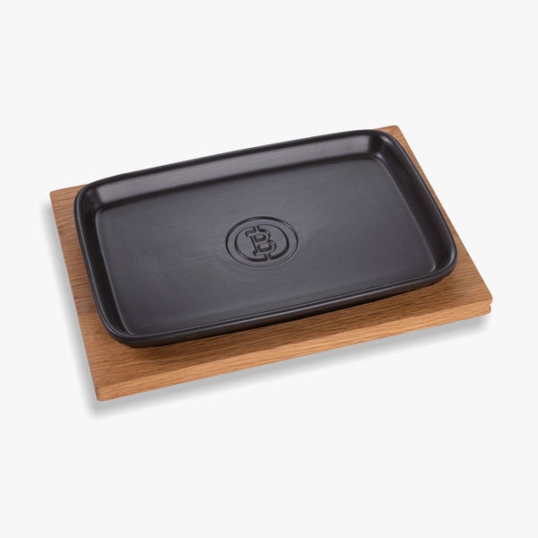 Rechteckige schwarze Servierplatte mit The Bastard Logo auf einem Holzbrett.