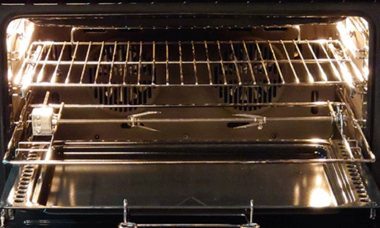 Innenraum eines Backofens mit Grillrost und Bratspieß auf einer Ebene, beleuchtet und mit zwei Lüftern in der Rückwand.