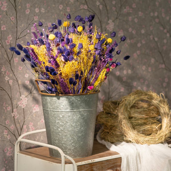 Dekorative Trockenblumen in einem Zinkeimer mit einem Strohkranz im Hintergrund.