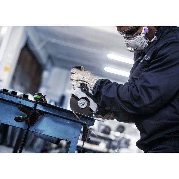 Eine Person arbeitet mit einem Winkelschleifer an einem Werkstück, wobei sie Schutzkleidung trägt.