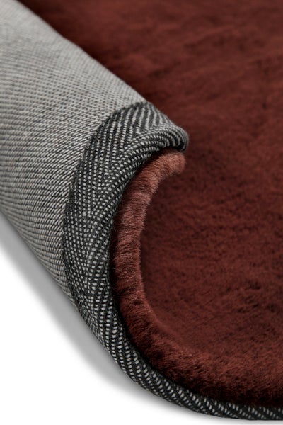 Brauner Kunstfellteppich mit gewebter Rückseite, Detailansicht der weichen Oberfläche und der strukturierten Unterseite.