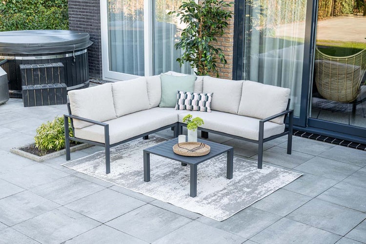 Garten-Lounge-Set mit L-förmigem Sofa aus Aluminium und Kissen, quadratischem Tisch und Außenteppich auf einer gepflasterten Terrasse.