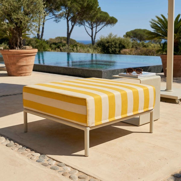 Quadratischer Outdoor-Hocker mit gelb-weiß gestreiftem Sitzkissen auf einer Terrasse am Pool.