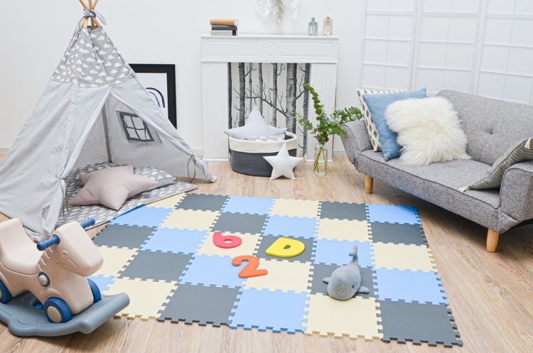 Helles, organisiertes Kinderzimmer mit karierter Schaumstoff-Spielmatte, grauem Tipi-Zelt, grauem Sofa und Schaukelpferd auf Holzboden.