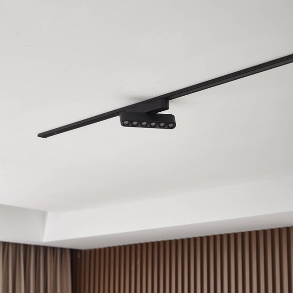 Modernes schwarzes Schienensystem mit einem flachen LED-Strahler montiert an einer weißen Decke vor einer Holzlamellenwand.