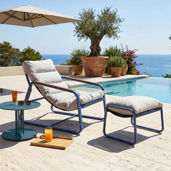Moderner Gartenlounge-Sessel mit passendem Hocker auf einer hellen, organisierten Terrasse am Pool. Metallgestell mit grauen Polstern.