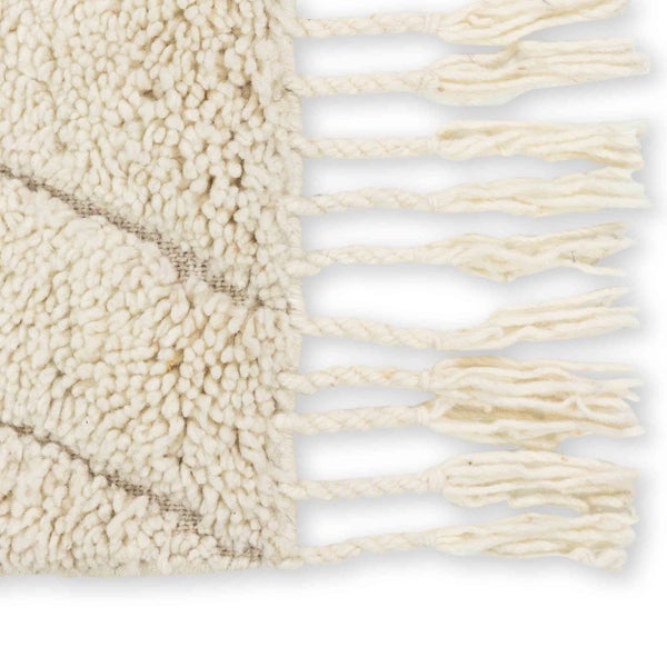 Detailaufnahme eines gewebten Hochflorteppichs mit geflochtenen Fransen am Rand.