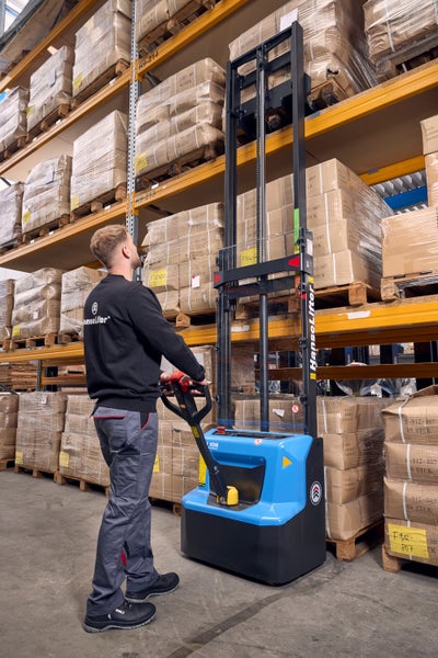 Mitarbeiter bedient einen HanseLifter Elektro-Hochhubwagen in einem Hochregallager mit palettierten Waren.