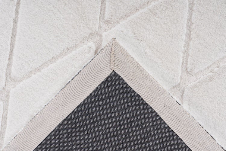 Nahaufnahme eines hellen Teppichs in Kunstfell-Optik mit geometrischem Muster und umgeklappter Ecke, die die Rückseite zeigt.