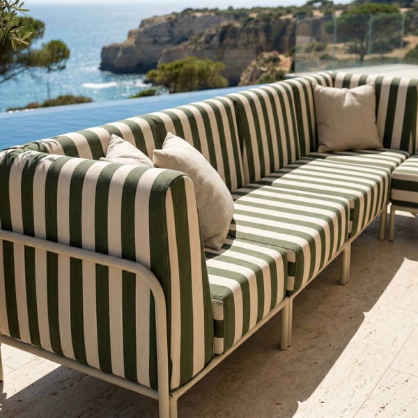 Modulares Gartensofa mit grün-weiß gestreiften Polstern und hellem Kissen auf einer Terrasse am Pool mit Meerblick.